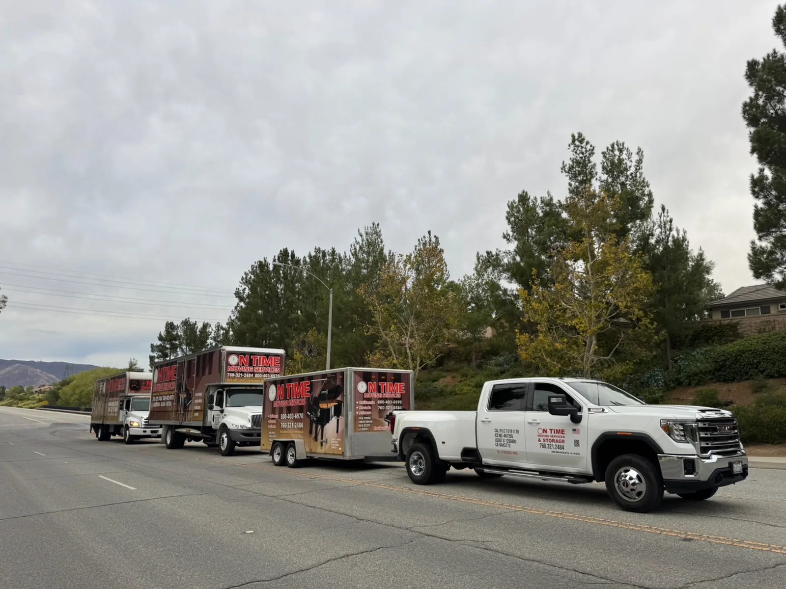 A line of company trucks and a trailer driving on a road as part of a move from Palm Desert to Banning, California.