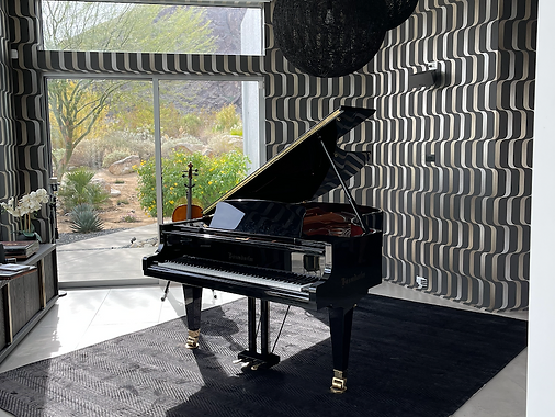 Black grand piano in a desert home interior with mountain views through sliding glass doors